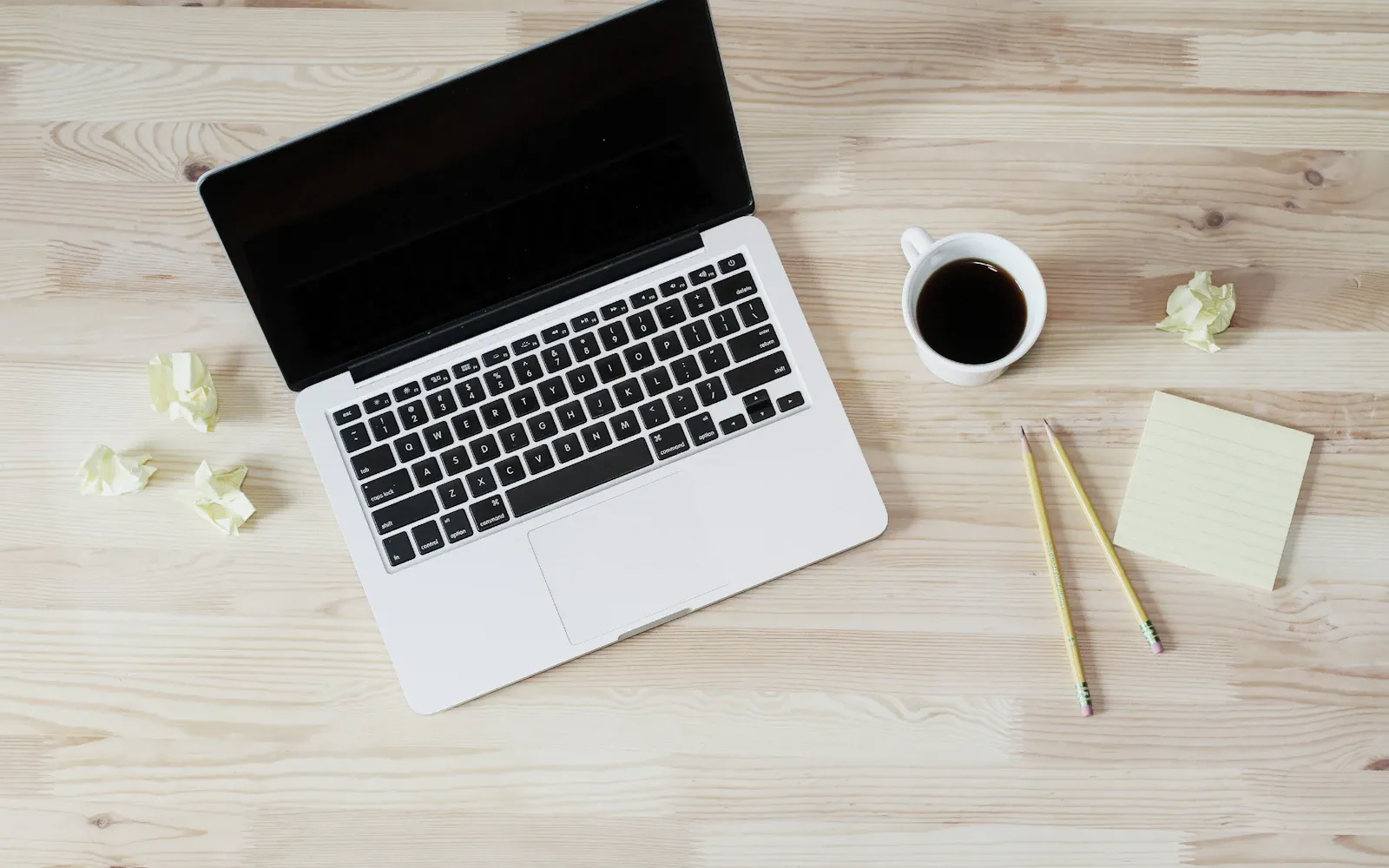 Bærbar computer, notesbog og kaffe på et lyst skrivebord